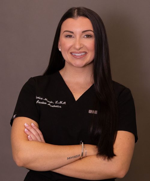 Smiling woman in black medical scrubs with long dark hair, arms crossed, neutral background