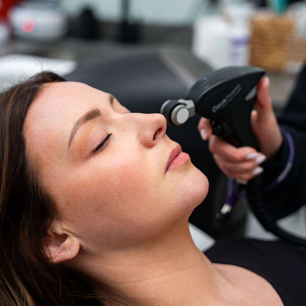 A woman receiving a microdermabrasion facial, handheld device applied near her nose while she rests.