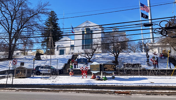 Snow-covered civic building on a hill with flags, holiday nutcracker decorations and memorial signs along the roadside