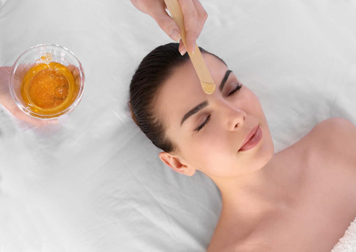 A woman receiving warm facial wax on her forehead with a spatula and bowl during a spa treatment
