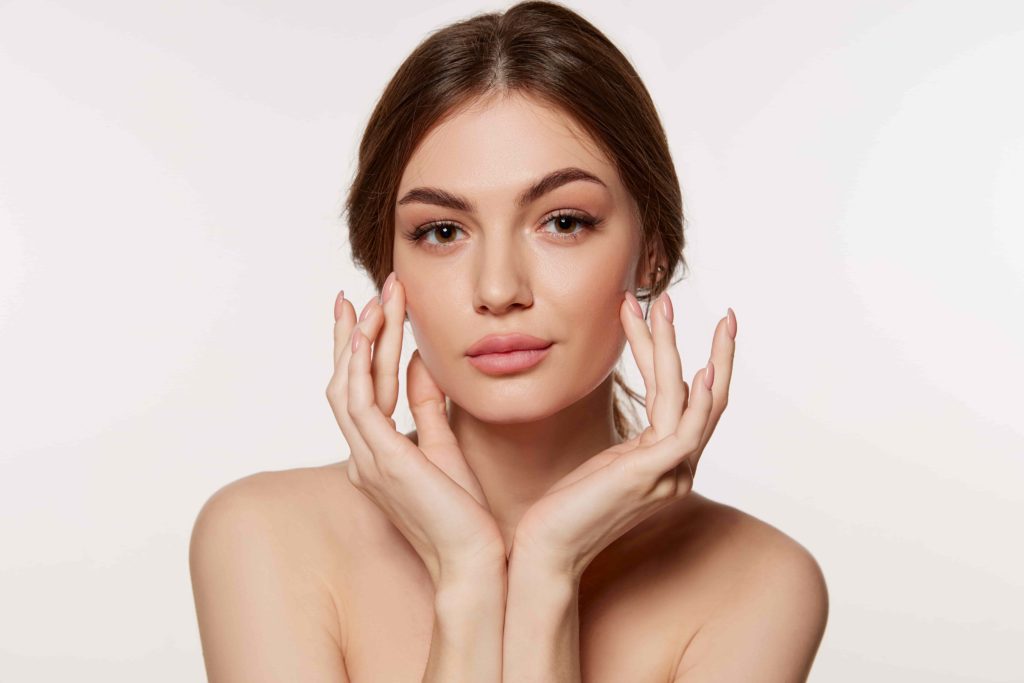 Close-up portrait of a woman with clear skin, natural makeup, hands framing face for skincare and beauty