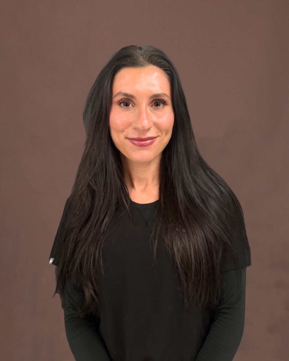 Portrait of a woman with long dark hair wearing a black top, smiling against a neutral brown background.