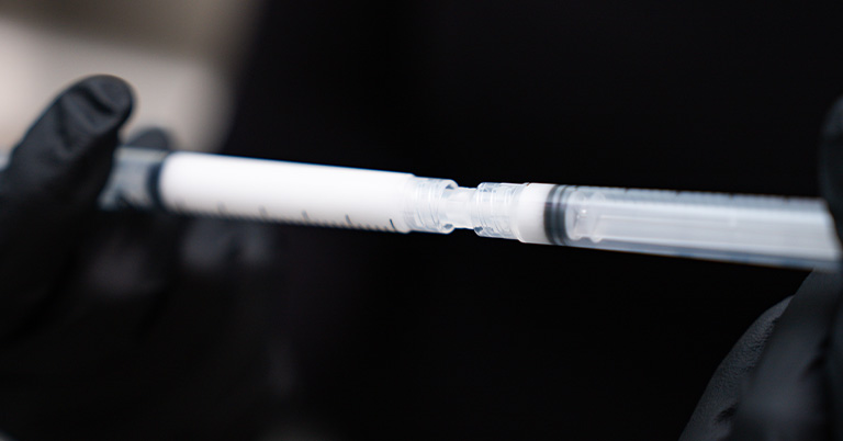 Close-up of a person wearing black gloves preparing a vaccine syringe with visible air bubbles in the barrel